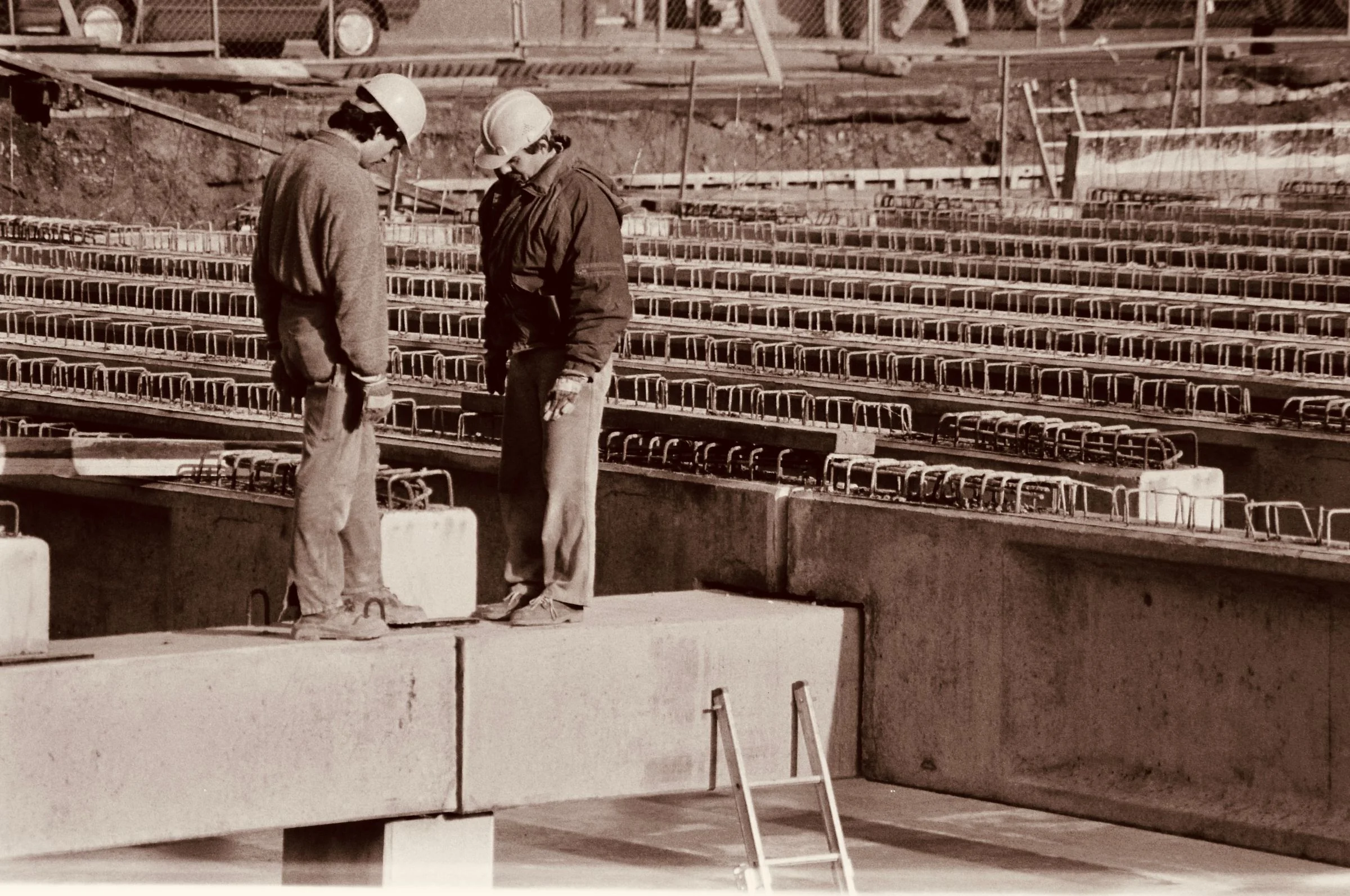 Two construction workers reviewing plans beside reinforced concrete works