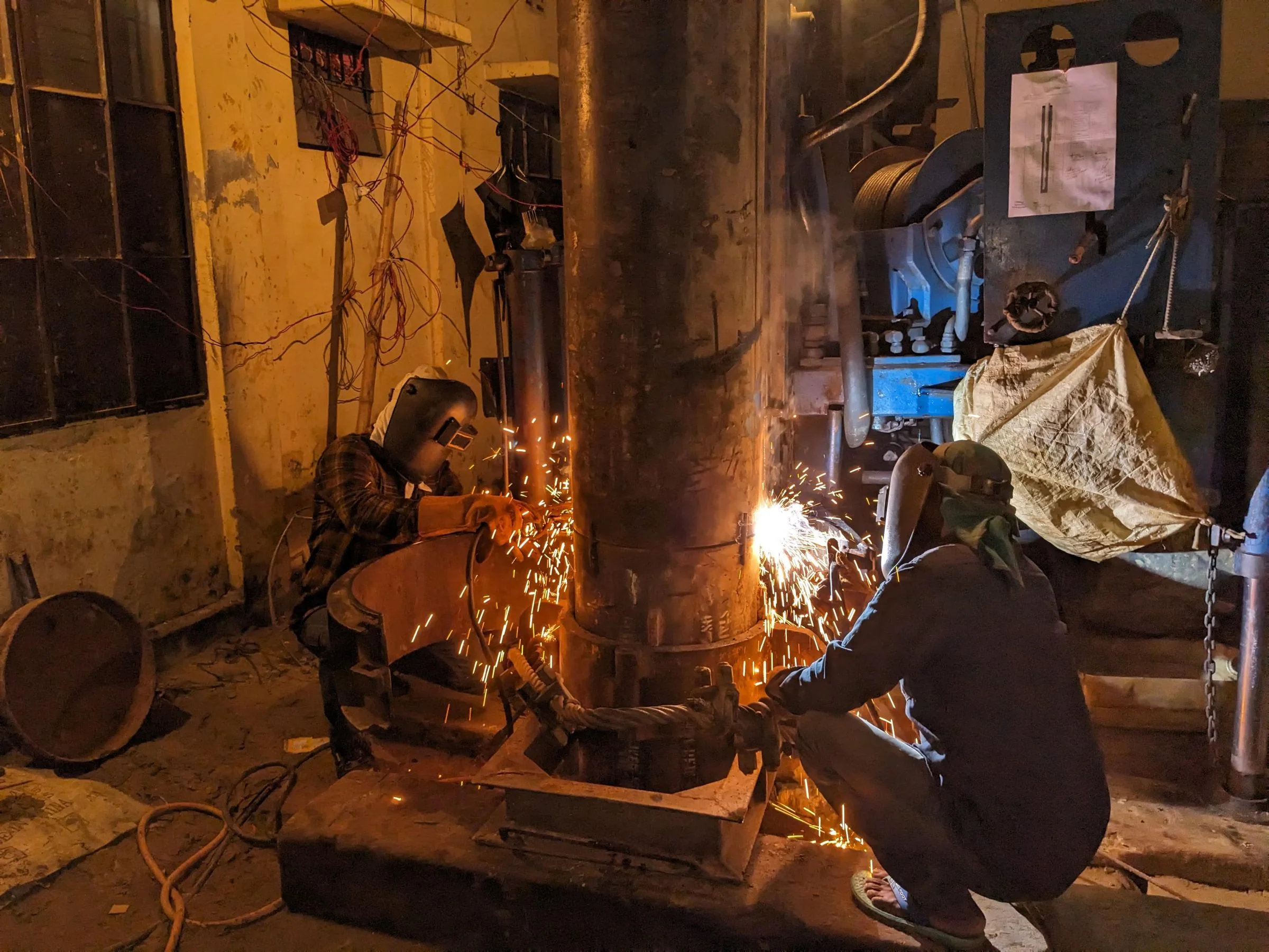 Welders fabricating large metal pipework inside an industrial workshop